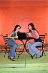 Two young adult women sitting in a cafe, having coffee and using a laptop. Vertical shot.