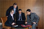 Ethnically diverse group of businessmen and a businesswoman look at a laptop computer screen. Horizontal shot.