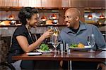African-American couple dining out. They are toasting with glasses of white wine and smiling. Horizontal shot.