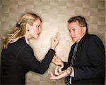 Caucasian mid-adult businesswoman angrily giving middle finger to middle-aged businessman who shrugs at her. Horizontal format.