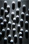 Close up of round white pills in a shaft of light, casting a shadow. Vertical shot.