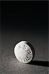 Close up of a round white aspirin standing on side on a gray background casting a shadow.