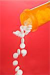 White round pills pouring from a yellow medicine bottle. Vertical shot. Isolated on red.