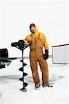 Young man in snow gear poses with an ice drill in a winter environment. Vertical shot.