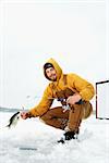 Young man pulls a fish out of a hole in the ice. He is holding a fishing rod and wearing snow gear. Vertical shot.