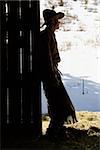 Silhouette of a cowboy leaning in a barn doorway, looking outside. Vertical shot.