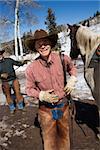 Man in a cowboy hat smiles next to a horse. Another man is standing in the background. Vertical shot.