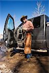 Man standing with a lariat next to the open door of a pickup truck. Vertical shot.