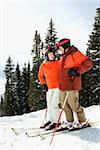 Skiers side by side on a snowy ski slope with trees in the background. Vertical shot.