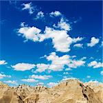 Mountain terrain in Badlands National Park, South Dakota, beneath blue sky and clouds. Square format.