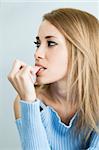 portrait of 30 years old woman biting her fingernails on cyan background. Vertical shape