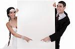 Bride and groom pointing at blank board over white background