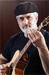 Portrait of a middle-aged man wearing a black beret and t-shirt and playing an acoustic guitar. He is looking at the camera. Vertical shot.