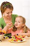 Eating healthy fruits is delicious and fun - woman and little girl enjoying a fresh dessert