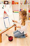 Little artist girl painting a house on a large sheet of paper