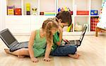 Kids busy using the computer sitting on the floor in their room