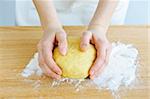 Hands kneading ball of dough with flour on cutting board