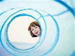 2-3 years old girl peeking from blue toy tunnel and grimacing. Horizontal shape, Copy space