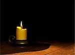 Burning candle on wooden table. Over black