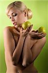 glamour shot of a nude young woman with two apple on green background looking down