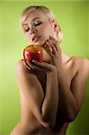 fashion and glamour shot of a dreaming nude young woman with red apple on green background