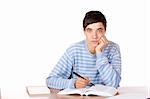 Young student is sitting on desk with open book and learns for his exams. He looks neutral into camera. Isolated on white.