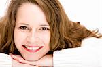 Young woman lying on floor with chin on hands is smiling happy into camera. Isolated on white.