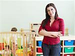 portrait of mid adult teacher in kindergarten. Little girls playing with toys in background. Horizontal shape, copy space