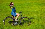 Young woman with a vintage bicycle relaxing on a green meadow