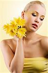 sweet and beauty blond girl wearing a yellow top keeping yellow flower and looking down. wellness concept