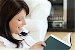 Attractive woman reading a book lying on a sofa at home