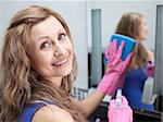 Charming woman cleaning a bathroom's mirror with a sponge and detergent spray