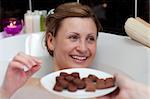 Bright woman eating chocolate while having a bath in a spa center