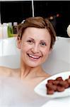 Radiant woman eating chocolate while having a bath in a spa center