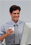Positive businessman holding a drinking cup sitting at his desk