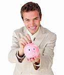 Smiling young businessman saving money in a piggy-bank against a white background
