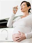 portrait of italian 6 months pregnant woman drinking water in kitchen. Vertical shape, copy space