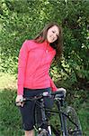 Young smiling woman walking down the park with bicycle