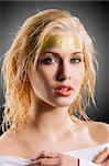 very cute blond girl with wet hair and a creative golden and shining make up on dark background