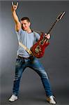 Portrait of a successful rock star holding an electric guitar and making a rock sign on a dark background