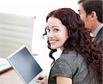 Positive businesswoman smiling at the camera while working at a laptop with her colleague