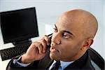 African American businessman sitting at office desk on cellphone.