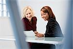 Businesswomen sitting at office desk discussing paperwork smiling.