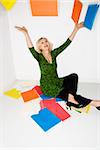 Caucasian middle aged businesswoman sitting on floor throwing stack of work folders into air.