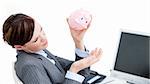 Upset businesswoman holding a piggy-bank in the office