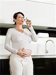 portrait of italian 6 months pregnant woman drinking water in kitchen. Vertical shape, copy space