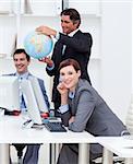 Happy manager holding a terrestrial globe with his team working at computers. Business concept.