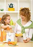 Healthy people - little girl and her mother - making fresh orange juice in the kitchen