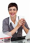 Charming Female executive drinking a coffee at her desk smiling at the camera