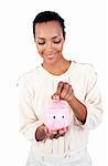 Young Afro-american businesswoman saving money in a piggybank against a white background